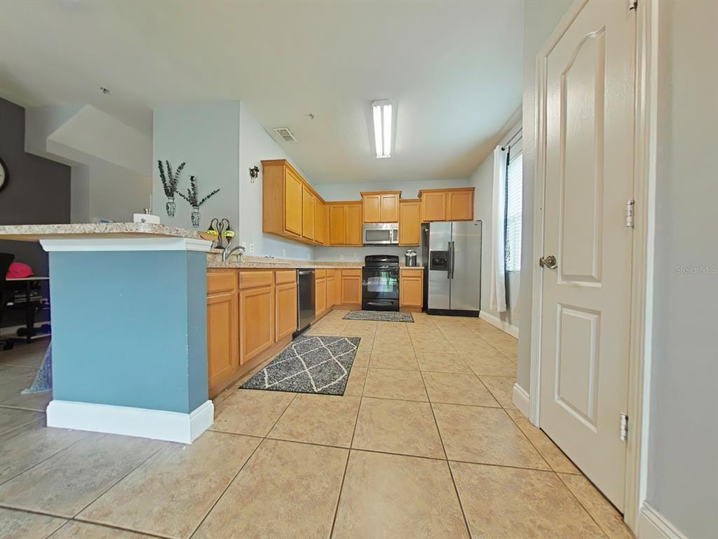 A kitchen features light wood cabinets, stainless steel appliances, and tan tile flooring — 15625 BOGGY OAK CIRCLE UNIT 108B, WINTER GARDEN, FL