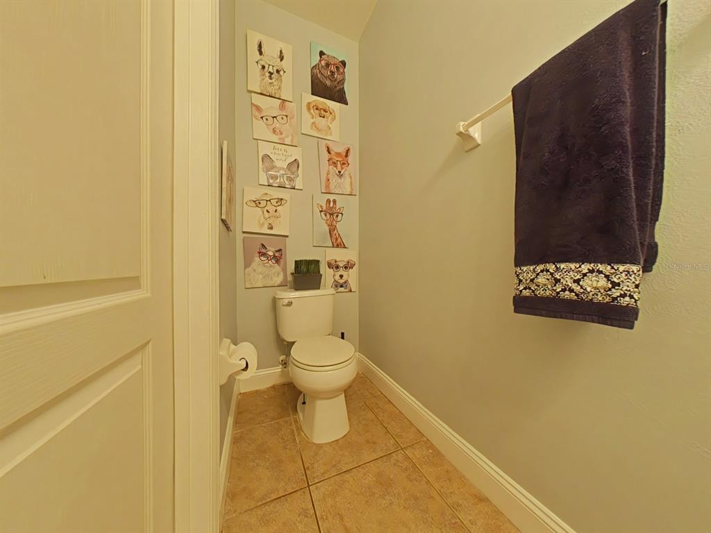 A small bathroom features a toilet, tile flooring, and a wall decorated with animal portraits — 15625 BOGGY OAK CIRCLE UNIT 108B, WINTER GARDEN, FL