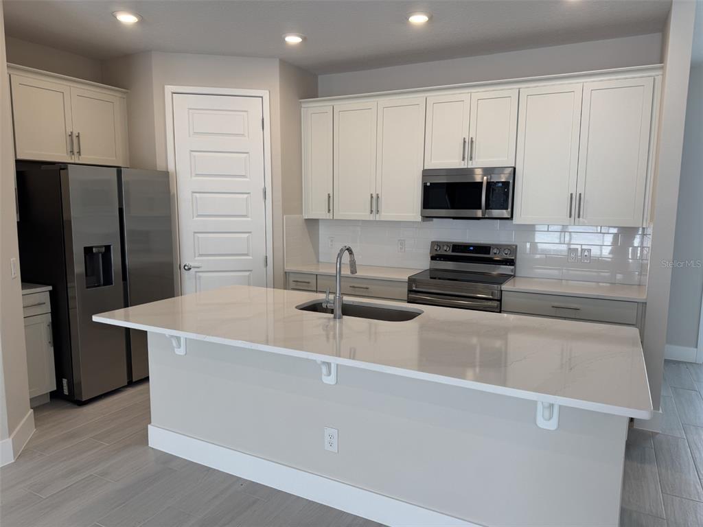 A modern kitchen features white cabinetry, stainless steel appliances, and a large quartz-topped island — 7921 SPECTRUM DRIVE, KISSIMMEE, FL