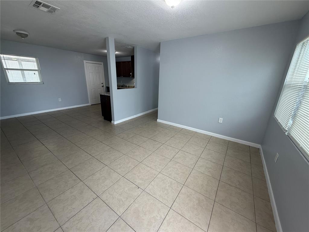 An empty room with light gray walls, beige tile flooring, and a partial kitchen wall — 613 CARVER DRIVE, LAKE WALES, FL