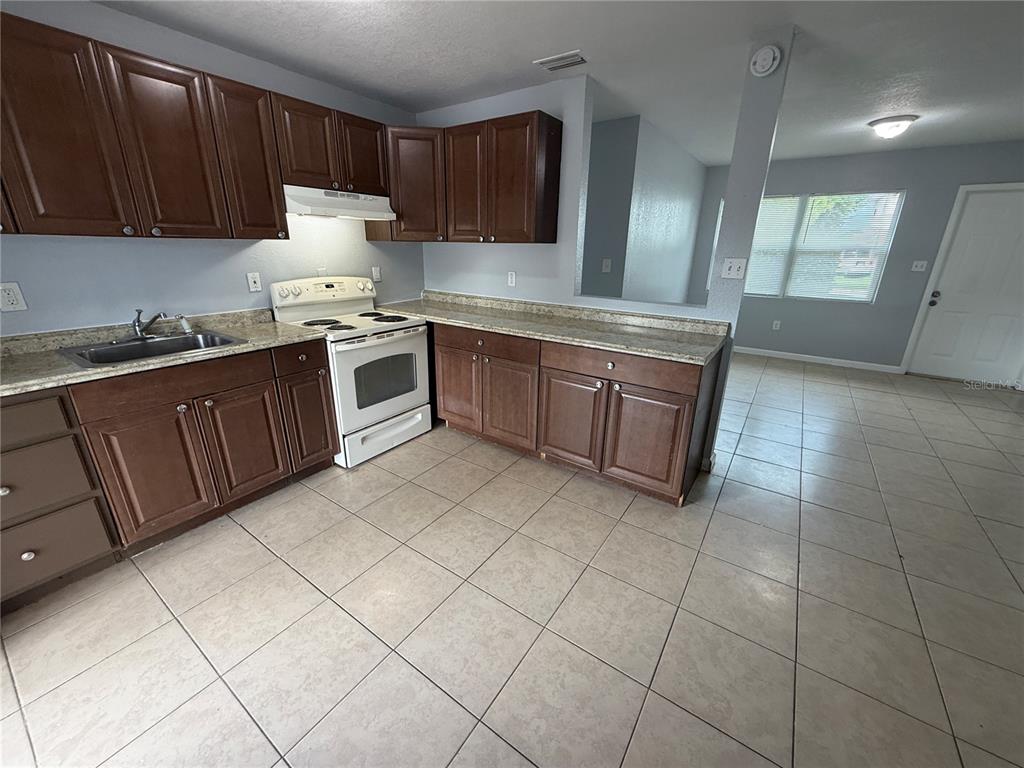 A kitchen features dark wood cabinets, white appliances, and light-colored tile flooring — 613 CARVER DRIVE, LAKE WALES, FL
