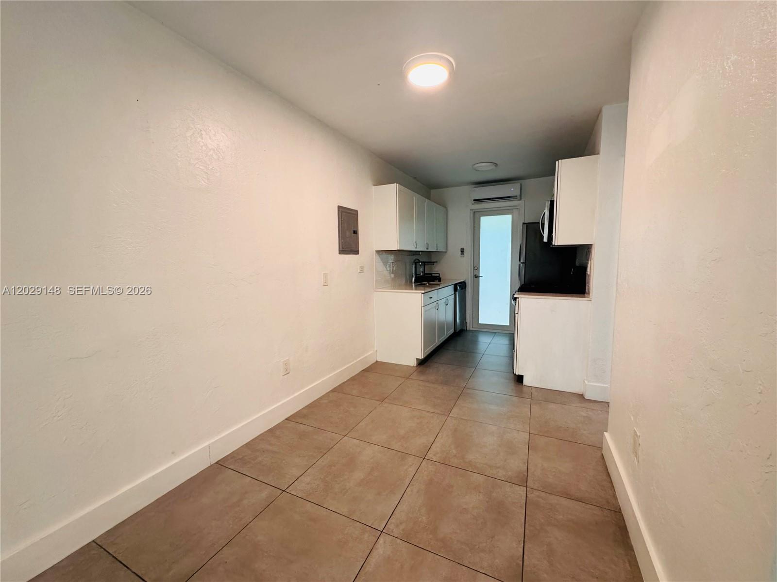 A small kitchen features white cabinets, tile flooring, and a glass door leading outside — 75 Washington Ave # 10, Miami Beach FL 33139, MIAMI BEACH, FL