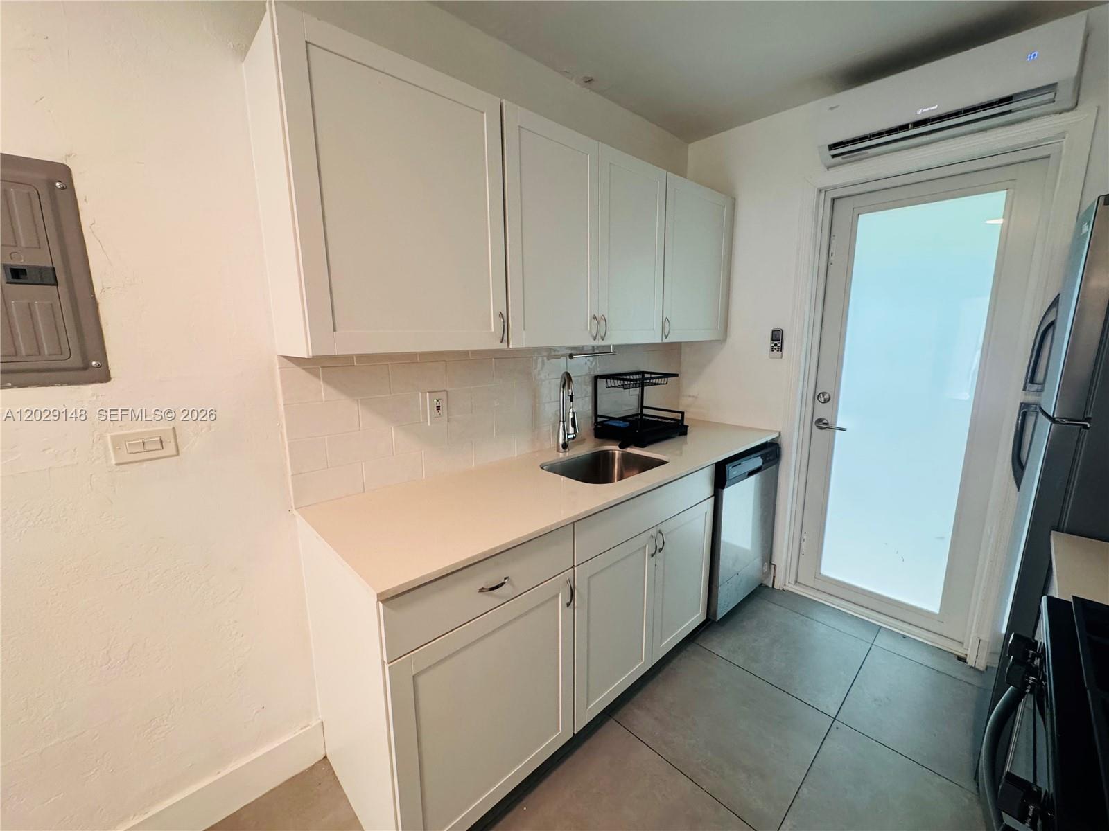 A small kitchen features white cabinets, a stainless steel sink, and a glass-paneled exterior door — 75 Washington Ave # 10, Miami Beach FL 33139, MIAMI BEACH, FL