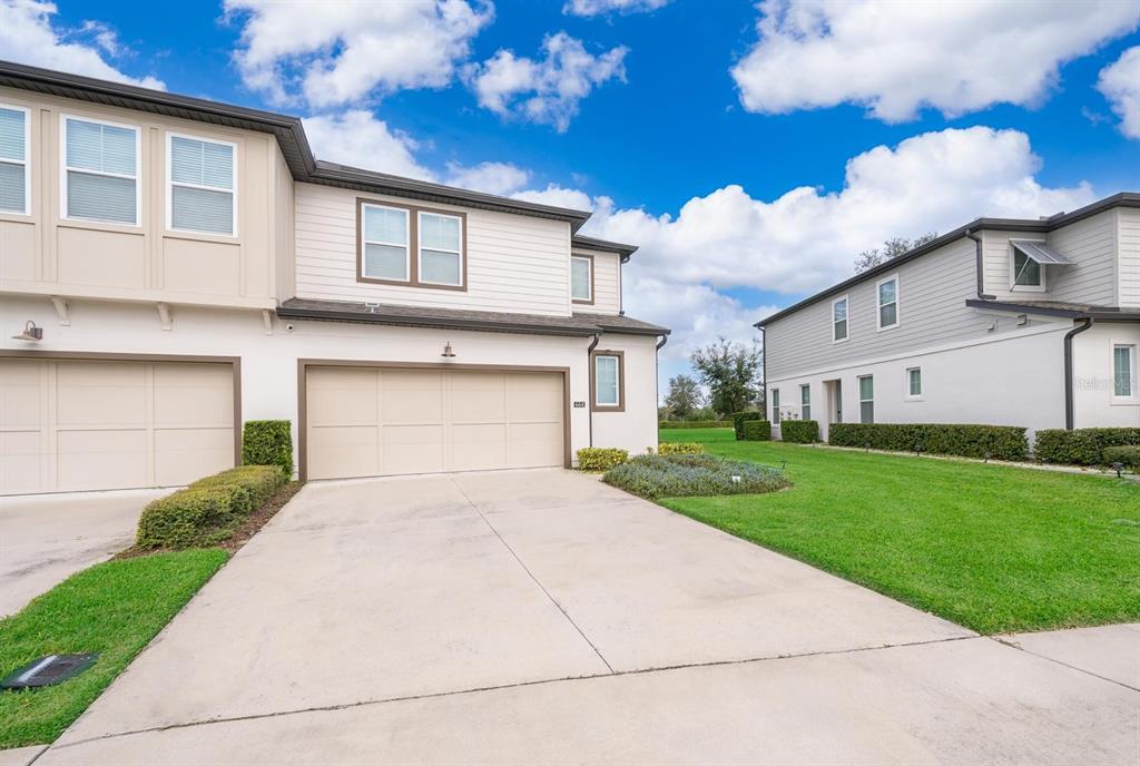 A two-story townhouse with a beige garage and a concrete driveway under a blue sky — 664 BENOI DRIVE, DAVENPORT, FL