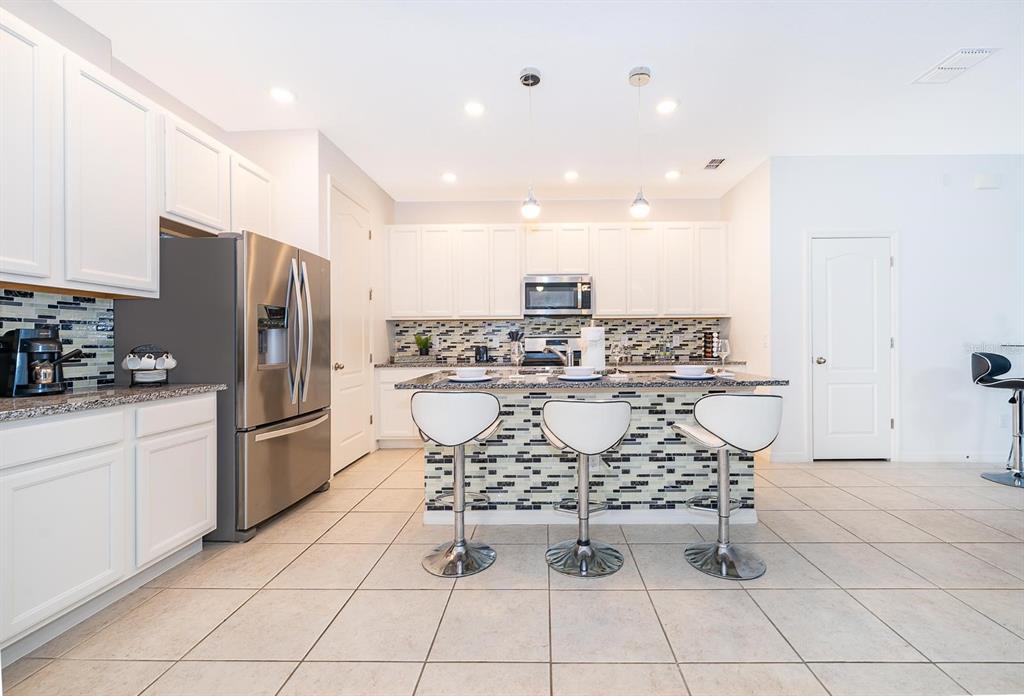 A kitchen features white cabinets, stainless steel appliances, a granite-topped island, and three bar stools — 664 BENOI DRIVE, DAVENPORT, FL