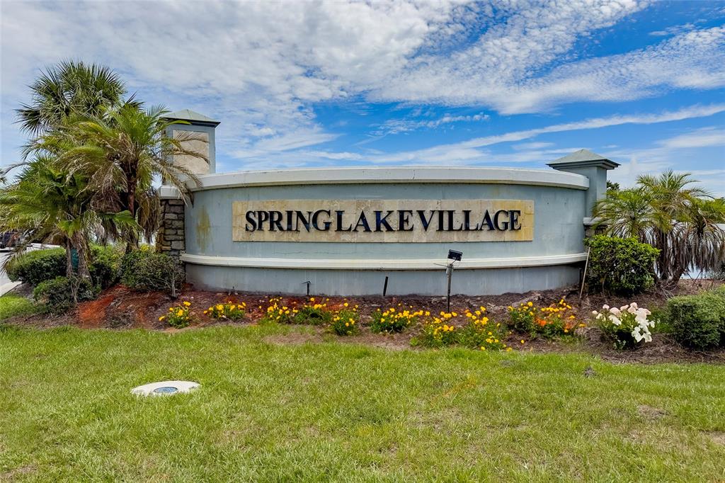 A curved monument sign for Spring Lake Village stands in a grassy landscape with palm trees — 3058 BAY LAUREL CIRCLE N, KISSIMMEE, FL