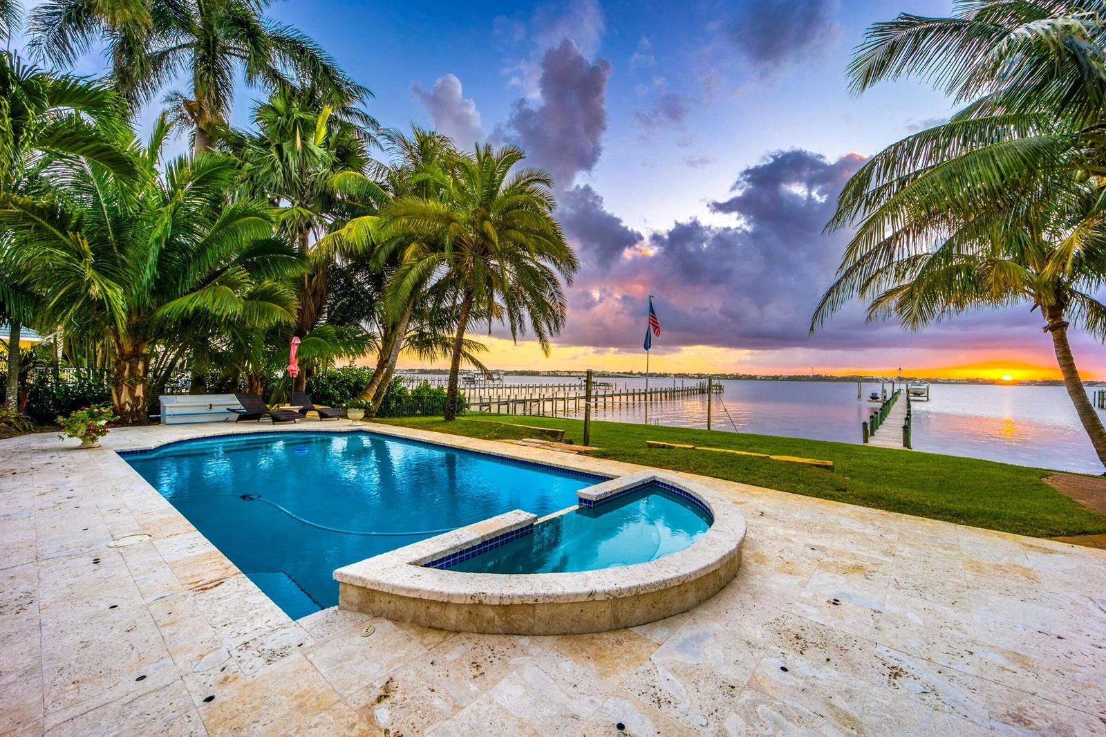 A swimming pool and spa overlook a waterfront dock at sunset with palm trees nearby — 2672 NW South Shore Road, Stuart FL 34994, STUART, FL