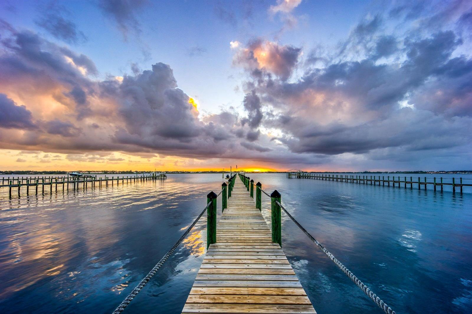 A wooden pier extends into calm water under a dramatic sunset sky with scattered clouds — 2672 NW South Shore Road, Stuart FL 34994, STUART, FL