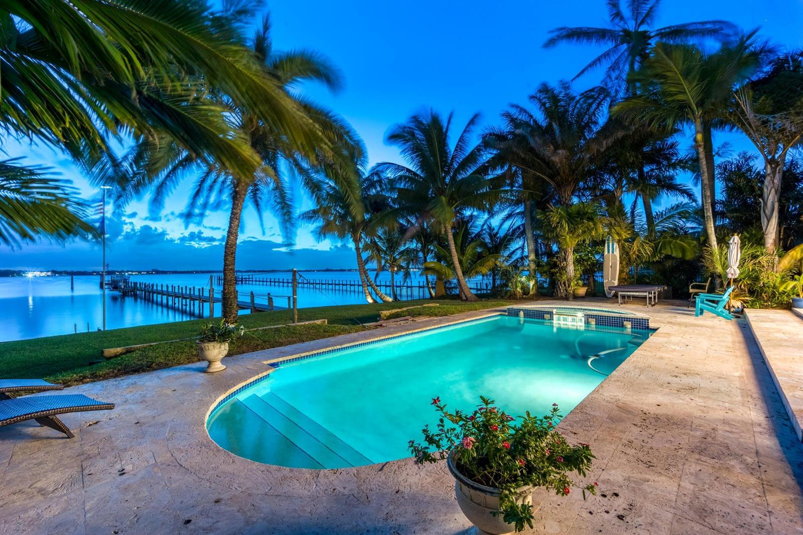 A swimming pool sits on a stone patio overlooking a dock and a calm bay — 2672 NW South Shore Road, Stuart FL 34994, STUART, FL