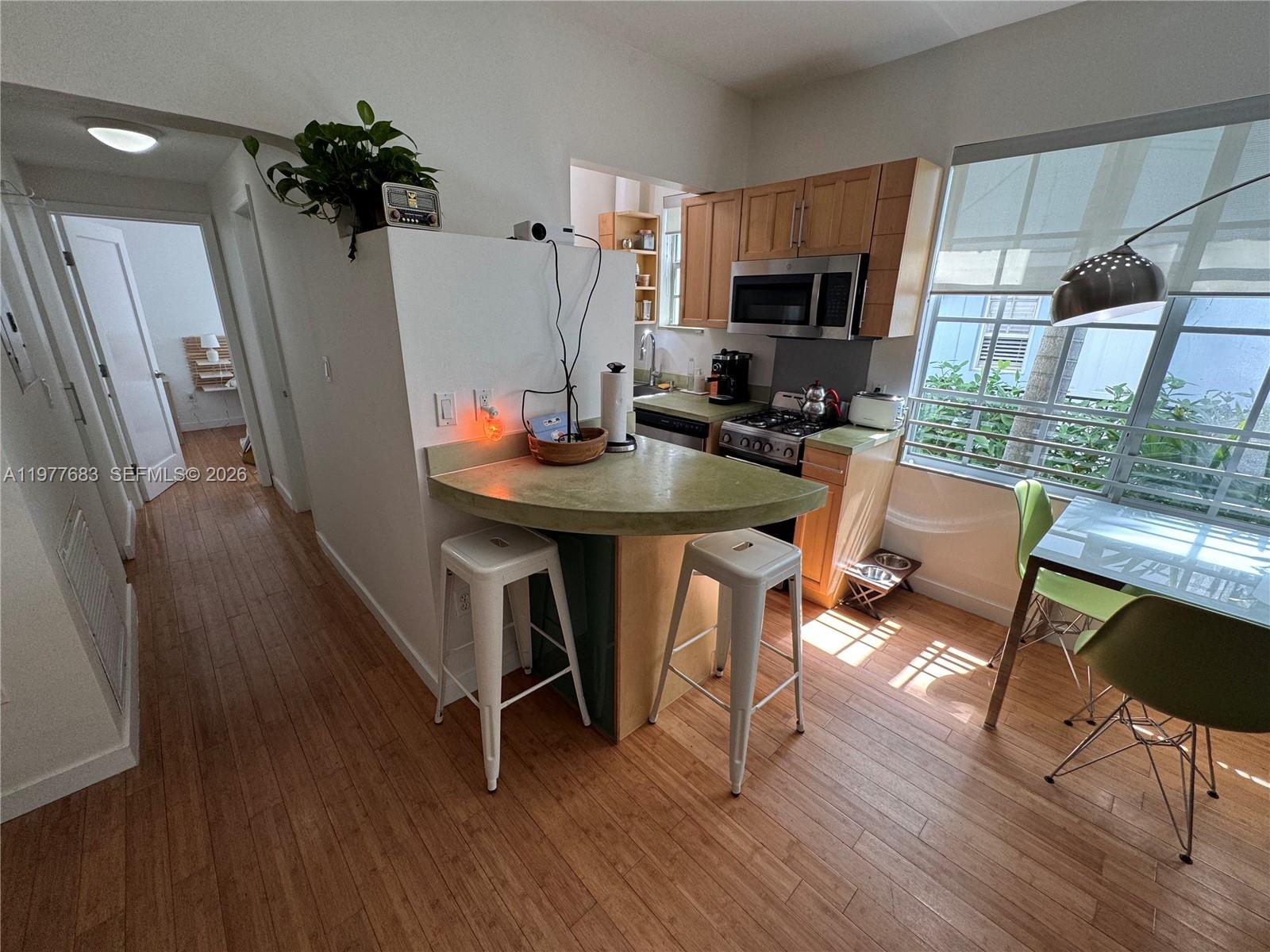 A kitchen features a curved breakfast bar, light wood cabinets, and a dining area — 815 Euclid Ave # 7, Miami Beach FL 33139, MIAMI BEACH, FL