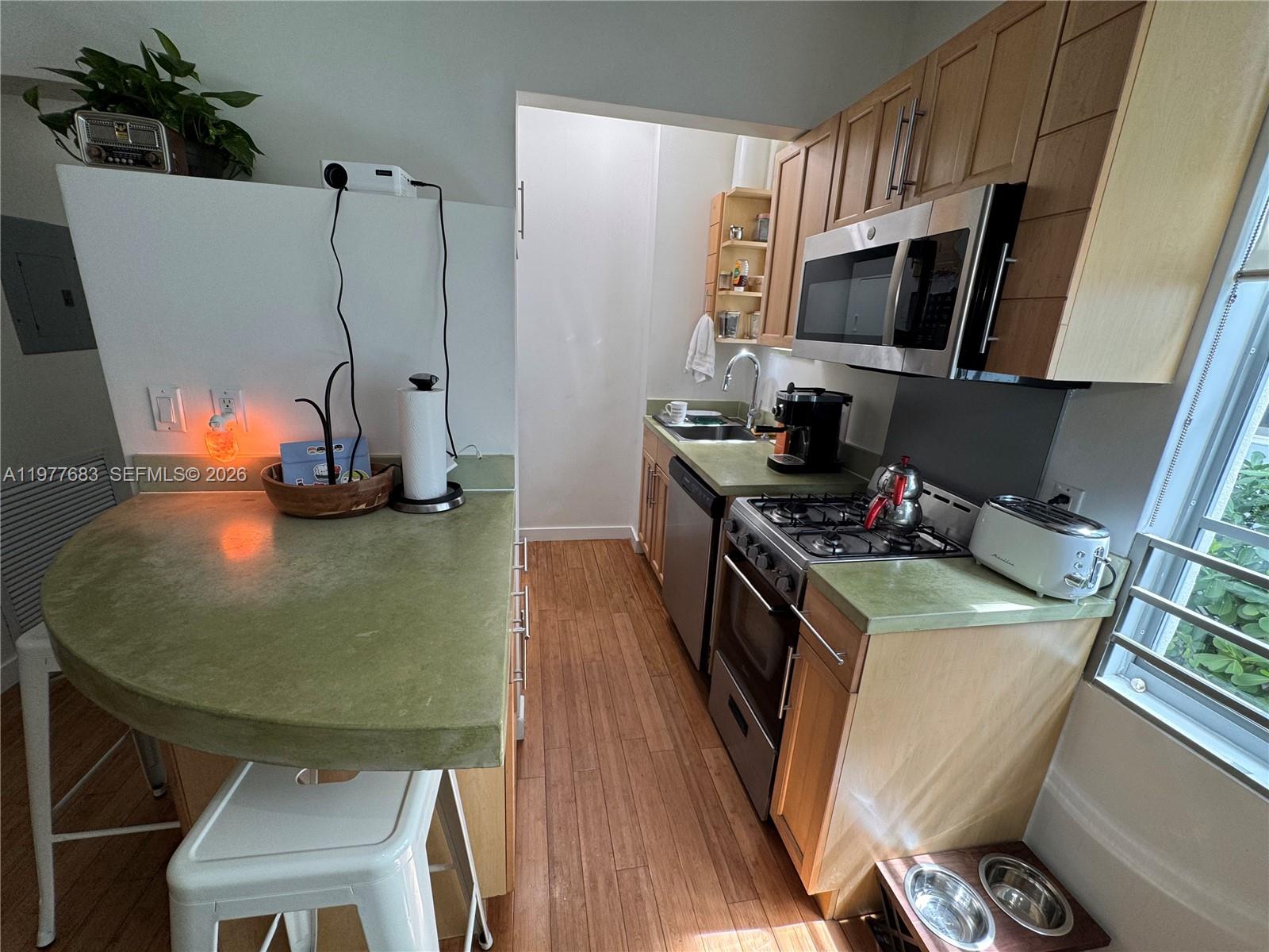 A small kitchen features light wood cabinets, green countertops, stainless steel appliances, and wood flooring — 815 Euclid Ave # 7, Miami Beach FL 33139, MIAMI BEACH, FL