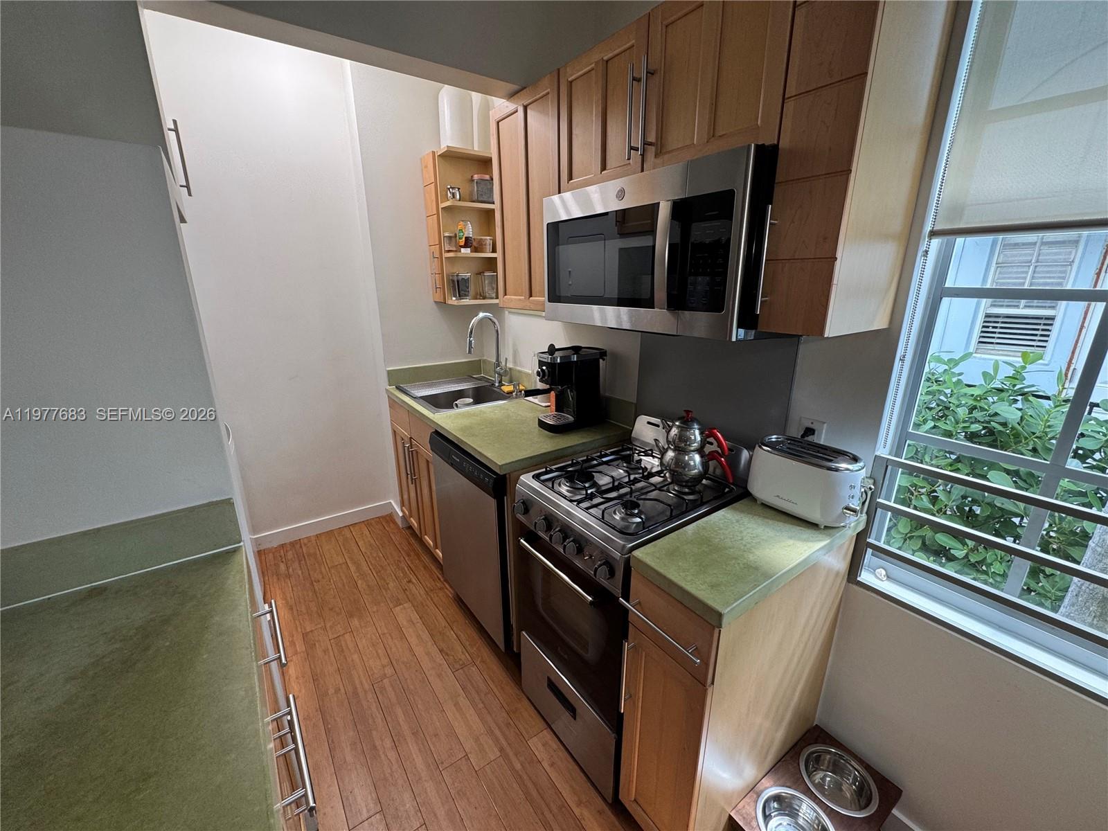 A galley kitchen features wood cabinets, green countertops, stainless steel appliances, and wood flooring — 815 Euclid Ave # 7, Miami Beach FL 33139, MIAMI BEACH, FL