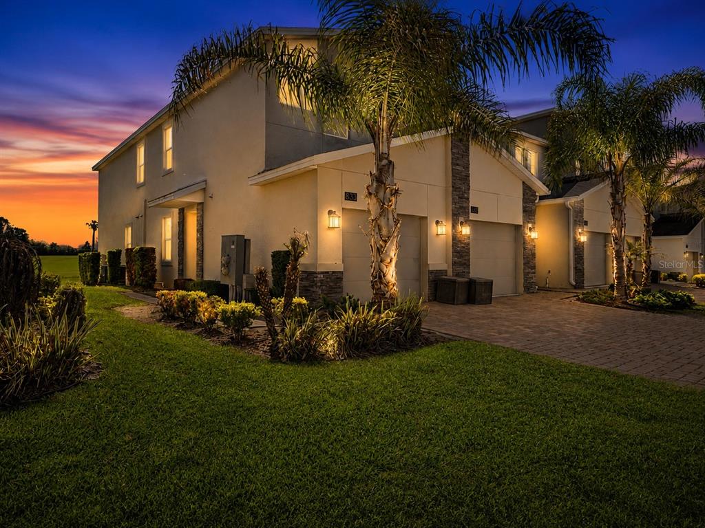 A two-story townhouse exterior at dusk with a paved driveway, palm trees, and green lawn — 833 OCEAN COURSE AVENUE UNIT 833, DAVENPORT, FL