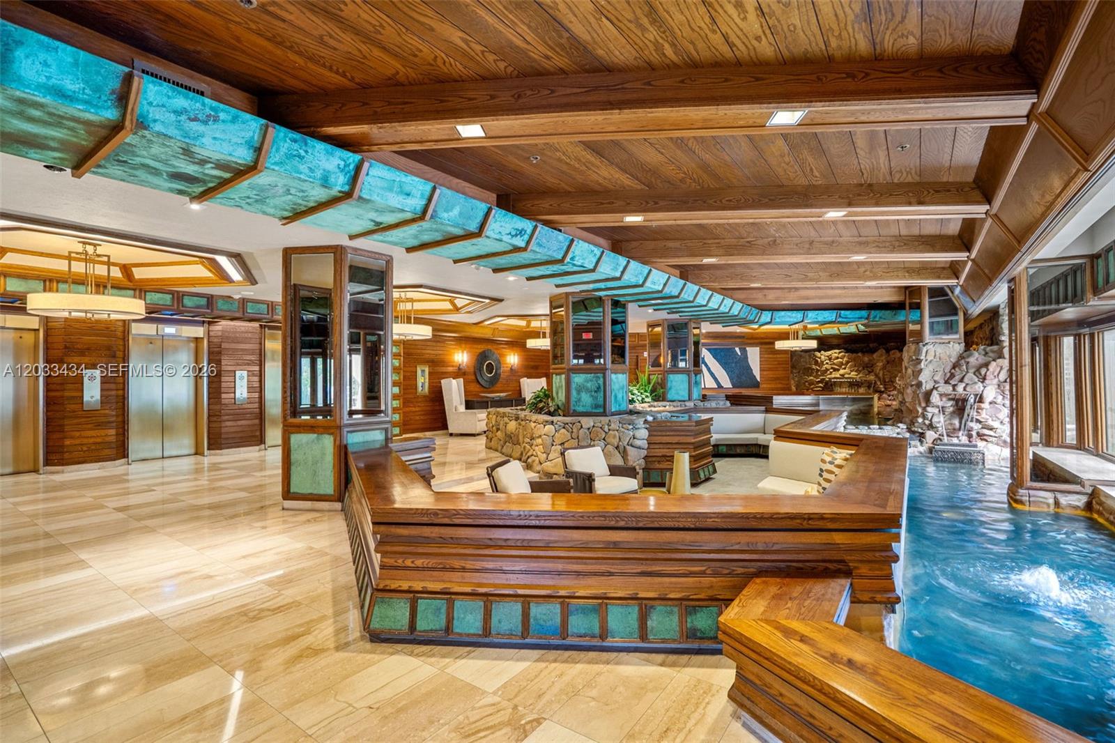 A lobby features wood-paneled ceilings, copper accents, stone pillars, and an indoor water feature — 1000 QUAYSIDE TER # 1604, Miami FL 33138, MIAMI, FL