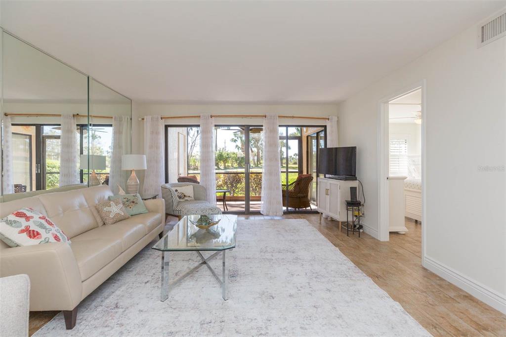 A living room features a beige sofa, glass coffee table, mirrored wall, and sliding glass doors — 5510 PUERTA DEL SOL BOULEVARD S UNIT 132, ST PETERSBURG, FL