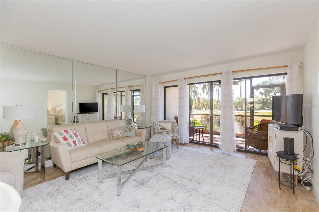 A living room features a beige sofa, glass coffee table, mirrored wall, and sliding glass doors — 5510 PUERTA DEL SOL BOULEVARD S UNIT 132, ST PETERSBURG, FL