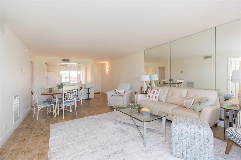 A living room with tile floors, a beige sofa, a glass coffee table, and mirrored walls — 5510 PUERTA DEL SOL BOULEVARD S UNIT 132, ST PETERSBURG, FL