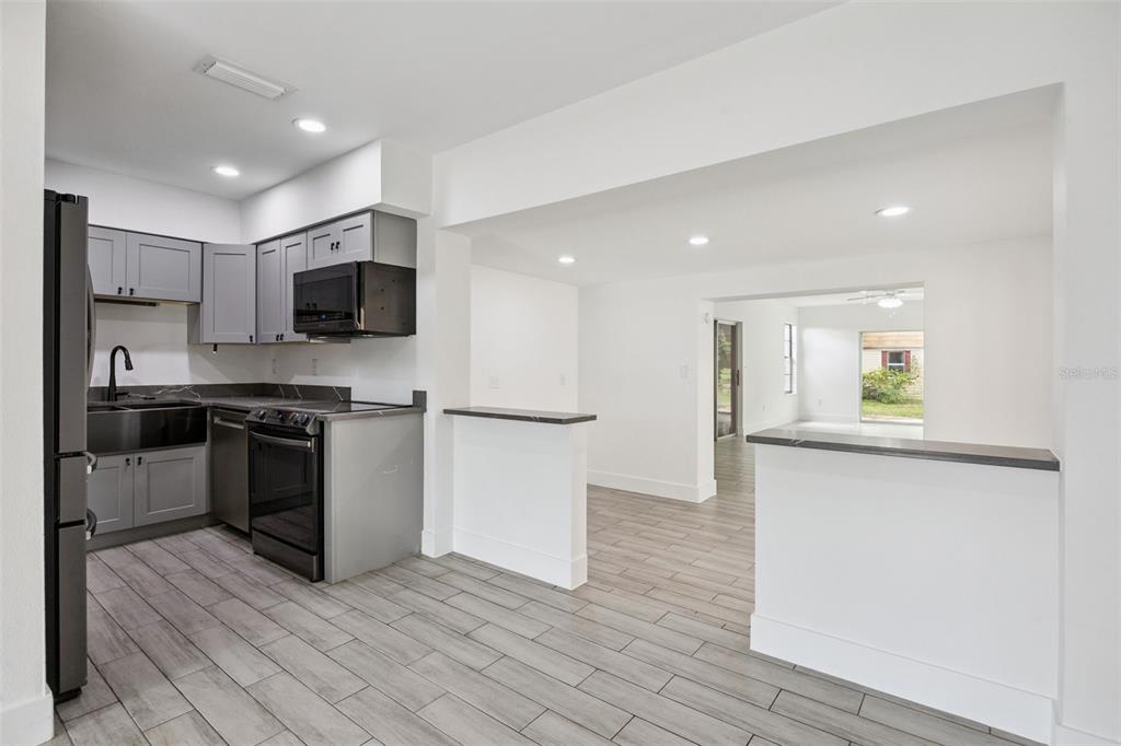 A kitchen with gray cabinets, black appliances, and a breakfast bar overlooking a living area — 204 W BUCHANON AVENUE, ORLANDO, FL