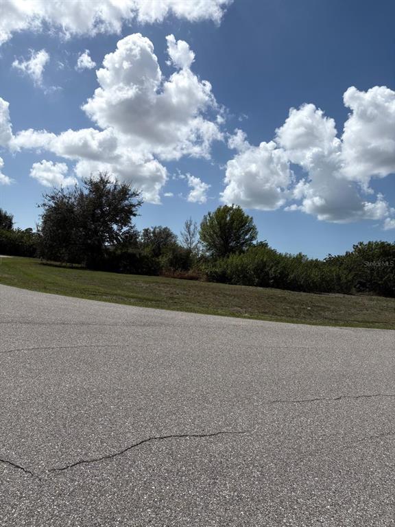 A paved road curves past a grassy lot with trees and bushes under a cloudy sky — 196 LINDA LEE DRIVE, ROTONDA WEST, FL
