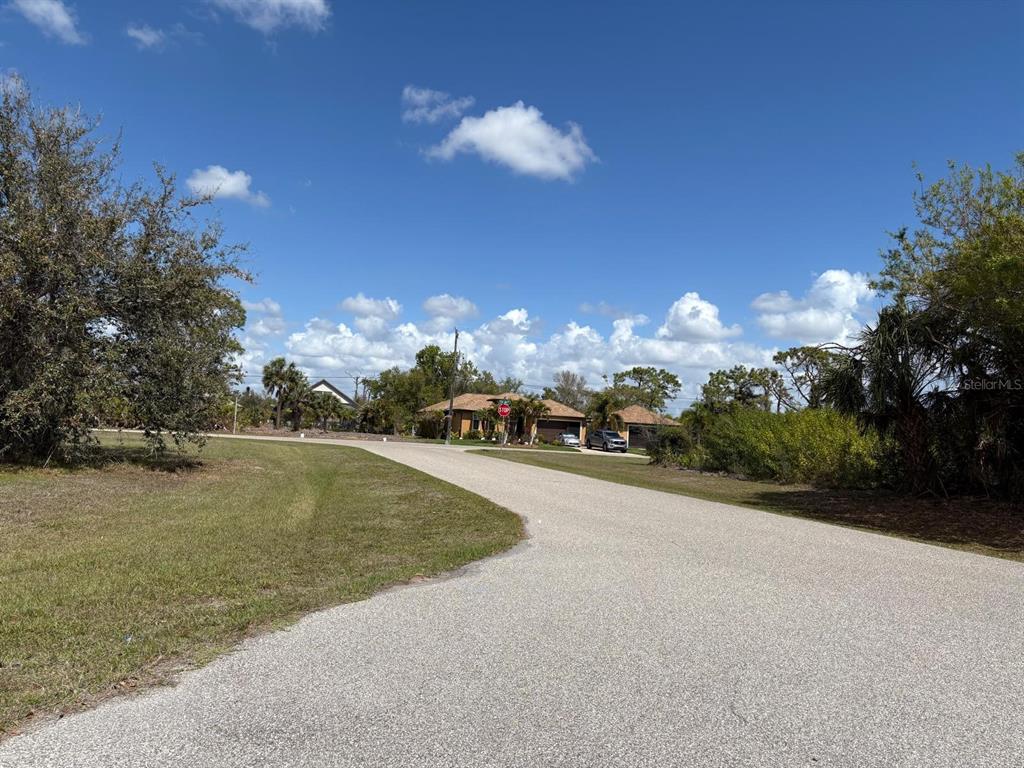 A paved road curves toward a house with a stop sign in a suburban neighborhood — 196 LINDA LEE DRIVE, ROTONDA WEST, FL