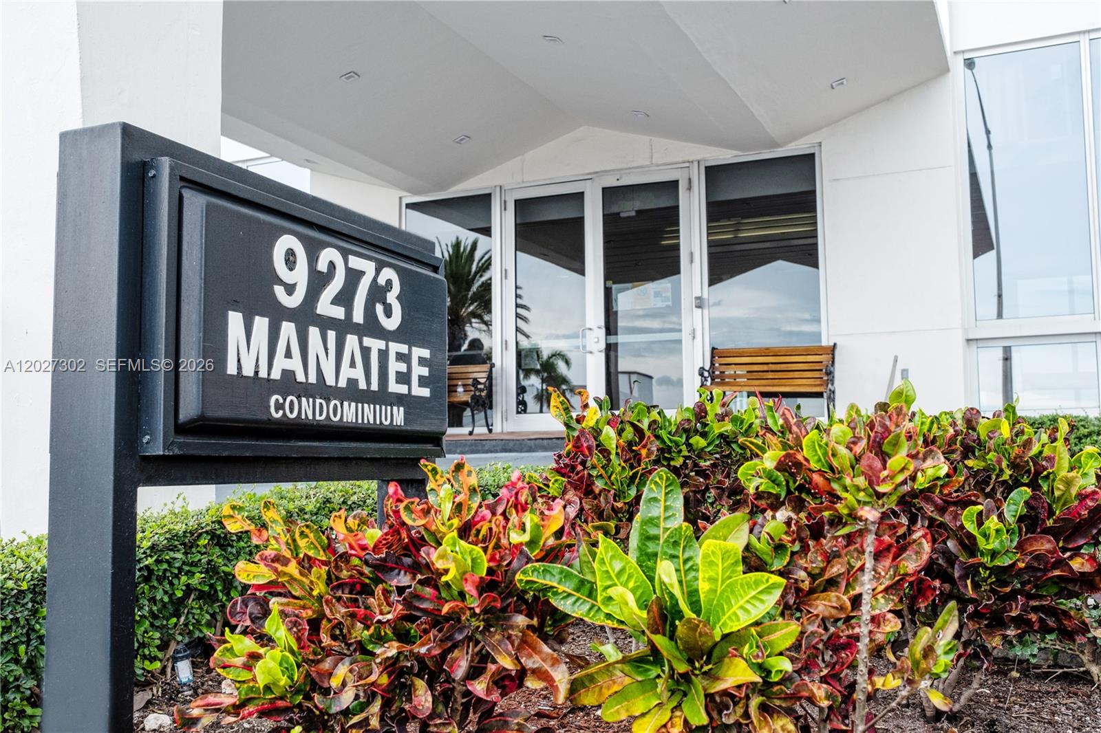 A sign for a condominium building stands in front of a glass entrance with landscaping — 9273 Collins Ave # 506, Surfside FL 33154, SURFSIDE, FL