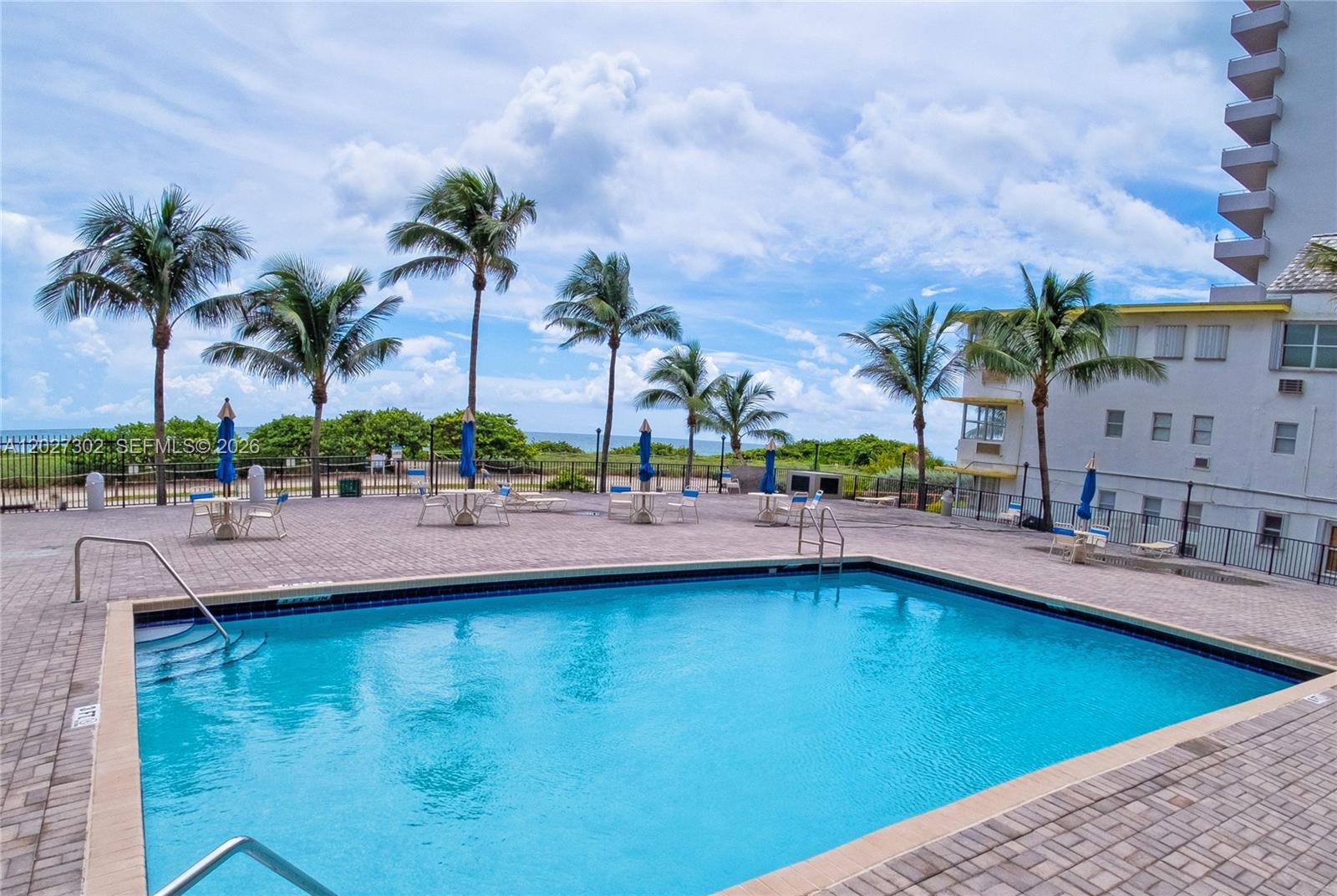 An outdoor swimming pool is surrounded by a paved deck, palm trees, and a building — 9273 Collins Ave # 506, Surfside FL 33154, SURFSIDE, FL