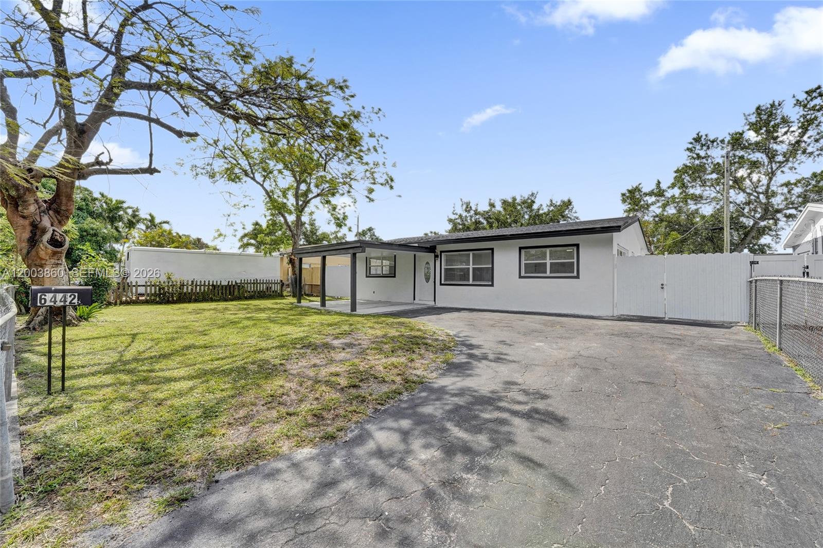 A white single-story house with a covered porch and a paved driveway sits on grass — 6442 Oak St, Hollywood FL 33024, HOLLYWOOD, FL