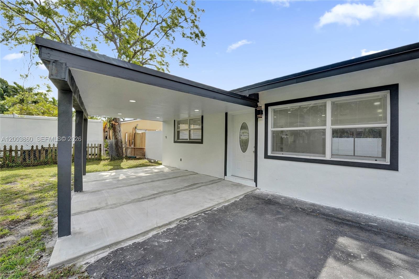 A white house exterior features a covered carport, a front door, and a large window — 6442 Oak St, Hollywood FL 33024, HOLLYWOOD, FL