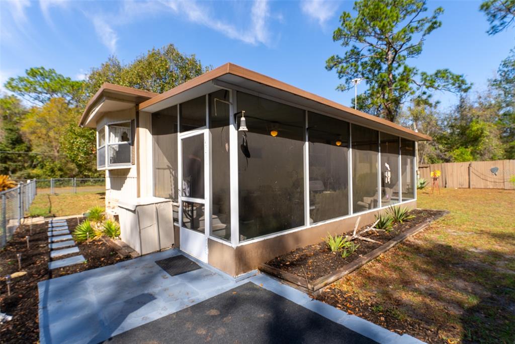 A mobile home with a screened-in porch and a paved walkway in a grassy yard — 14881 NE 147TH AVENUE, FORT MC COY, FL