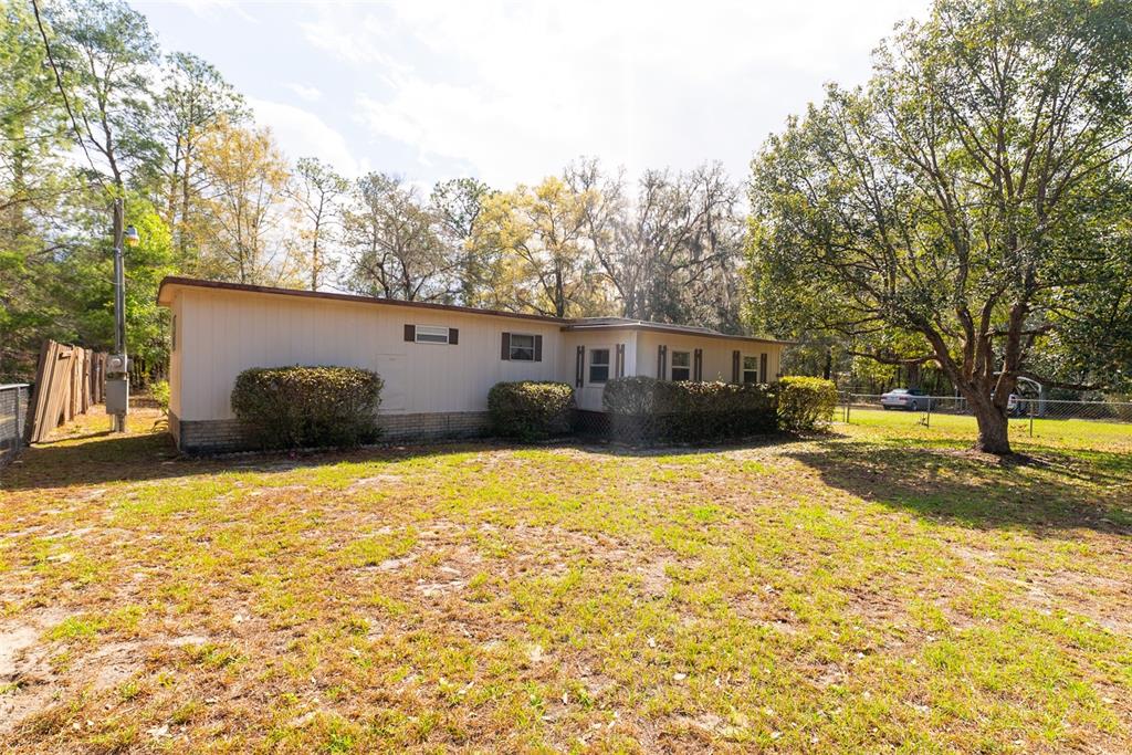A single-story house with light-colored siding and a brick base sits on a grassy lot — 14881 NE 147TH AVENUE, FORT MC COY, FL