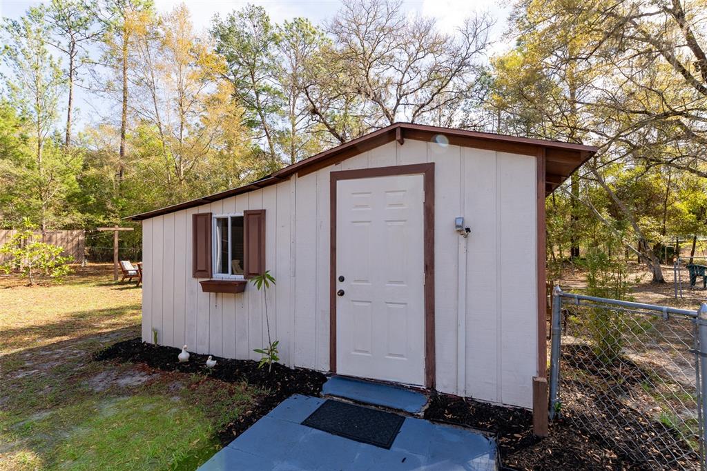 A small, light-colored shed with a single door and a window sits in a yard — 14881 NE 147TH AVENUE, FORT MC COY, FL