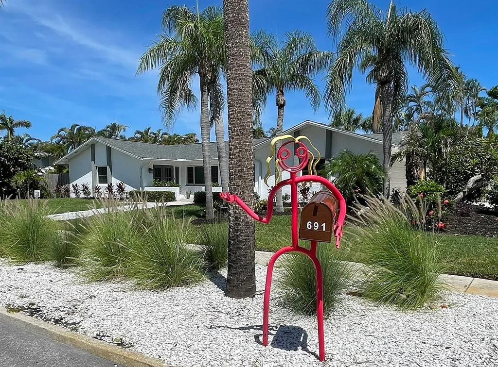 A whimsical red stick-figure mailbox stands in a landscaped front yard before a white house — 691 RUSSELL STREET, LONGBOAT KEY, FL