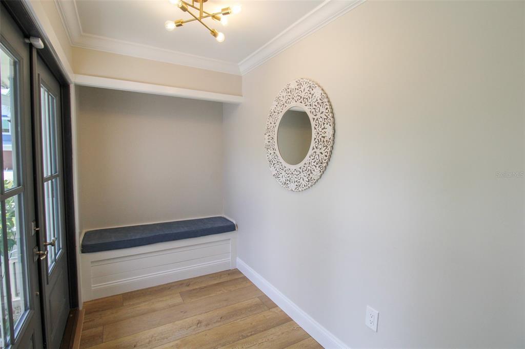 An entryway features a built-in bench with a blue cushion, a decorative mirror, and wood flooring — 691 RUSSELL STREET, LONGBOAT KEY, FL