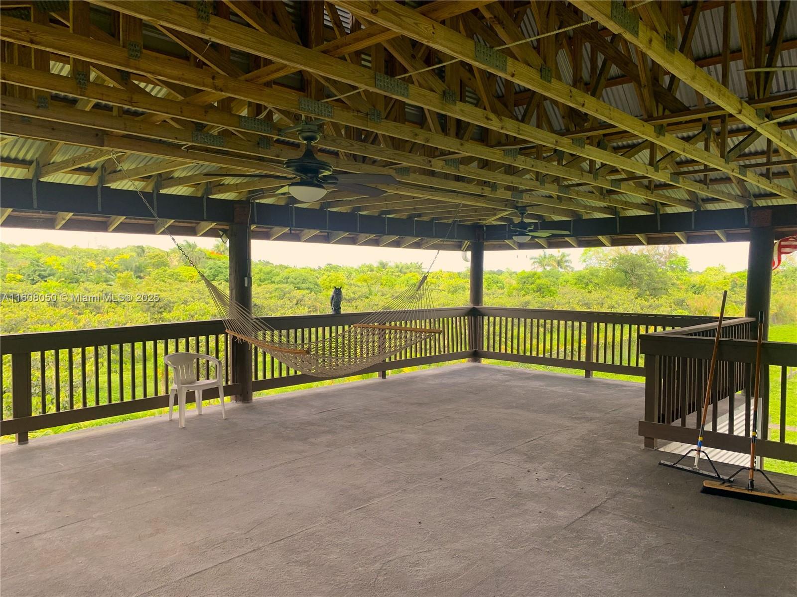 A covered wooden deck features a hammock, ceiling fans, and a view of lush greenery — 22750 SW 154th ave, Miami FL 33170, MIAMI, FL