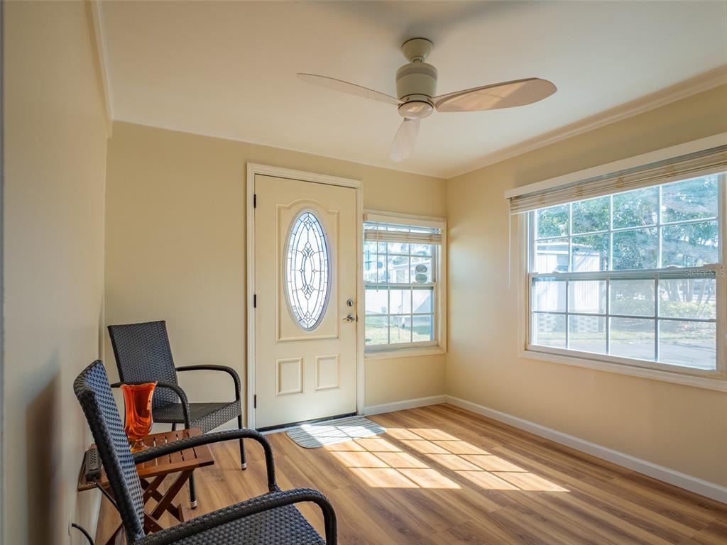 A sunroom with wood-look flooring, two wicker chairs, a ceiling fan, and a front door — 401 DENICE DRIVE UNIT 401, SEMINOLE, FL