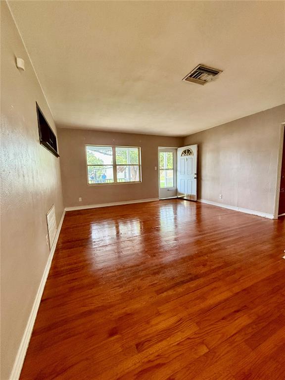 An empty living room features hardwood floors, a large window, and an exterior door — 1731 BALDWIN DRIVE, ORLANDO, FL