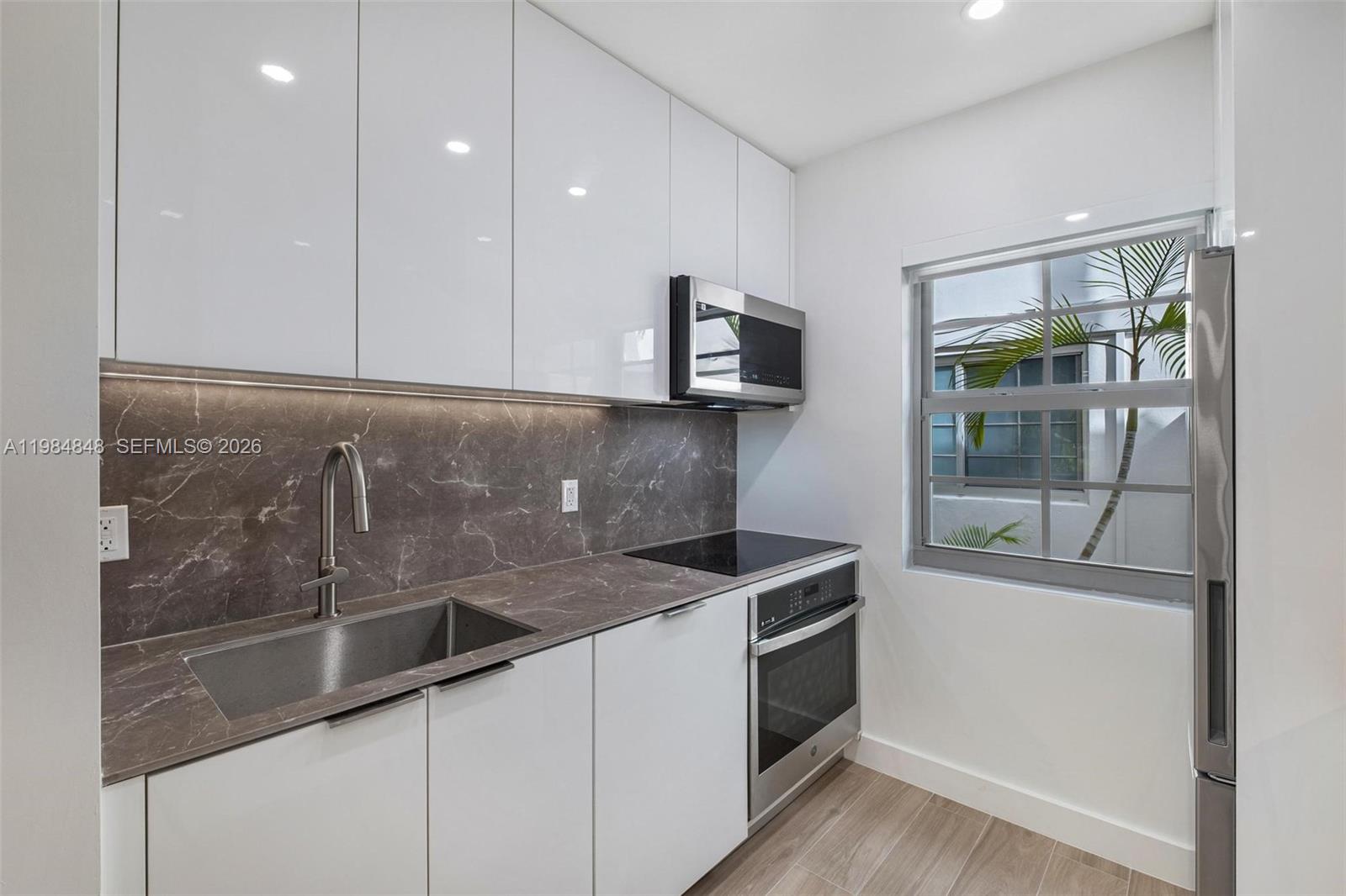 A modern kitchen features white cabinets, a dark marble backsplash, stainless steel appliances, and a window — 1610 Michigan Ave # 2, Miami Beach FL 33139, MIAMI BEACH, FL