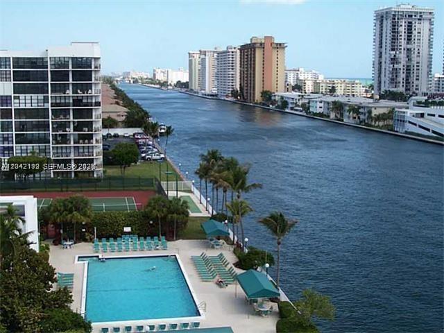 An aerial view shows a swimming pool, tennis court, and canal lined with high-rise buildings — 800 Parkview Dr # 1018, Hallandale Beach FL 33009, HALLANDALE BEACH, FL