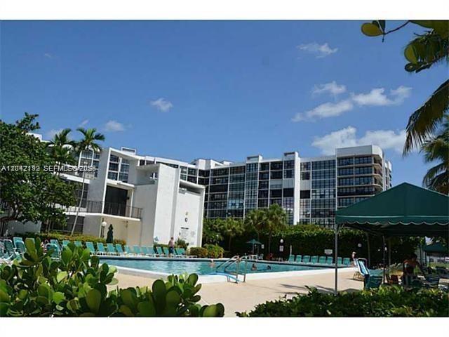 A swimming pool sits in front of a multi-story apartment building under a blue sky — 800 Parkview Dr # 1018, Hallandale Beach FL 33009, HALLANDALE BEACH, FL