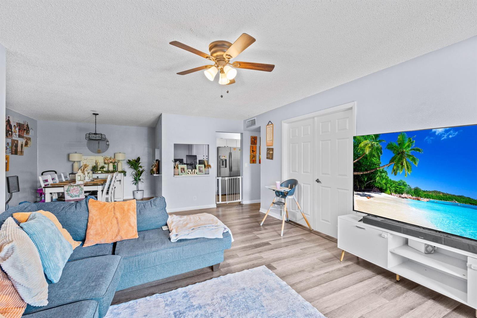A living room features a blue sectional sofa, a large television, and light wood flooring — 723 Sunny Pine Way # H2, FL 33415, FL