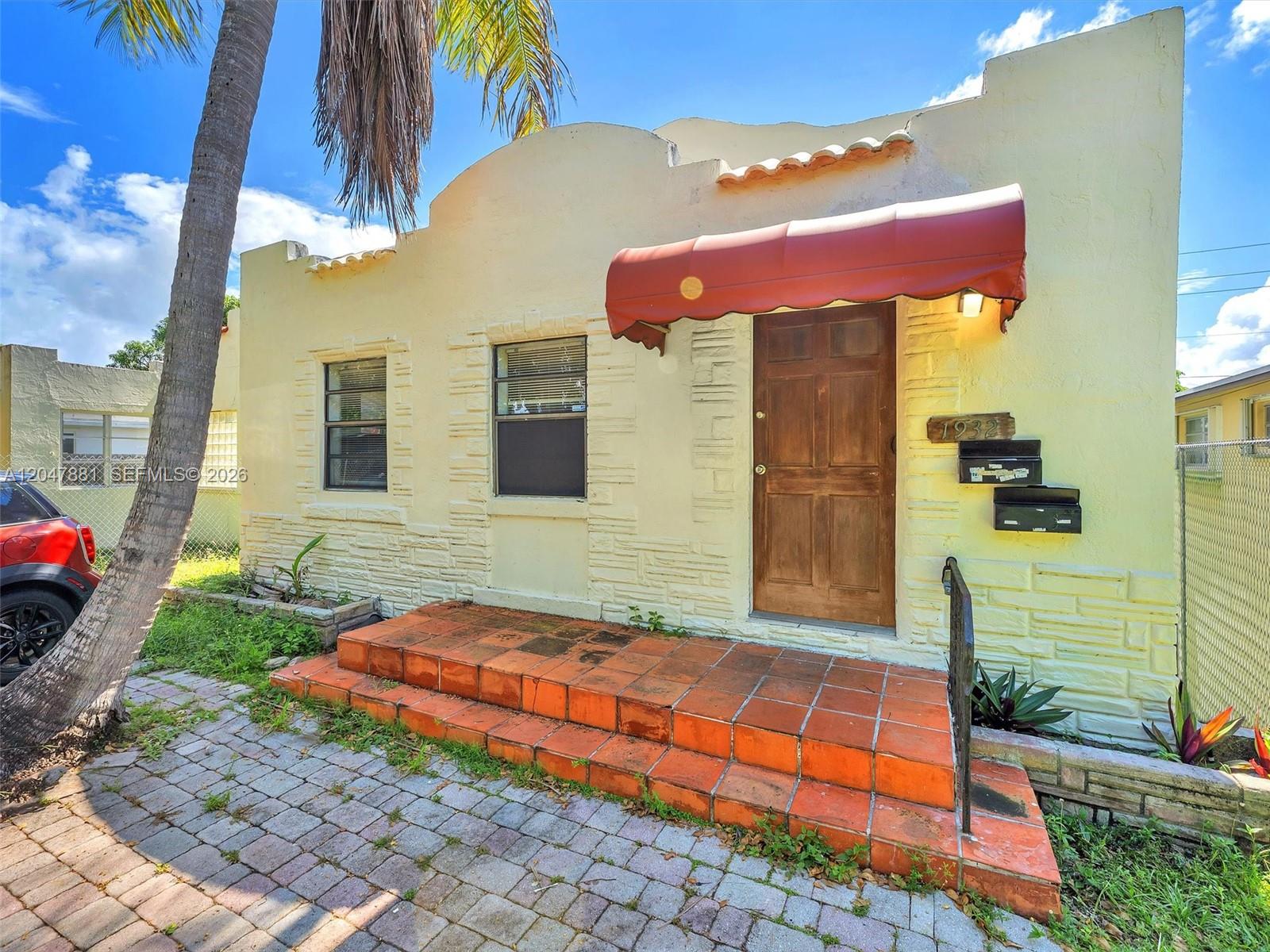A yellow stucco house features a red fabric awning over the front door and steps — 1932 Dewey St, Hollywood FL 33020, HOLLYWOOD, FL
