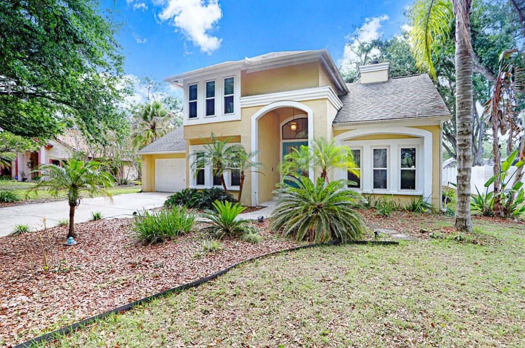 A two-story yellow house with a front-facing garage, arched entryway, and landscaped front yard — 6214 FARTHING STREET, TAMPA, FL