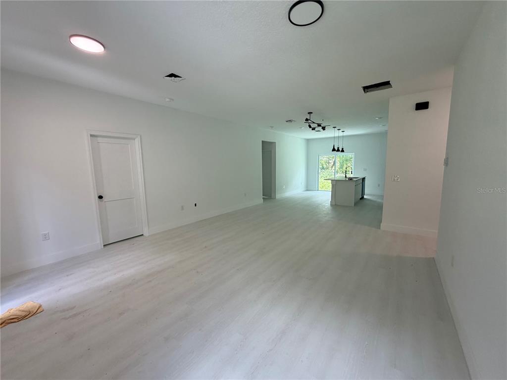 An open-concept living area features light wood-look flooring, white walls, and a distant kitchen island — 13542 SW 114TH PLACE, DUNNELLON, FL