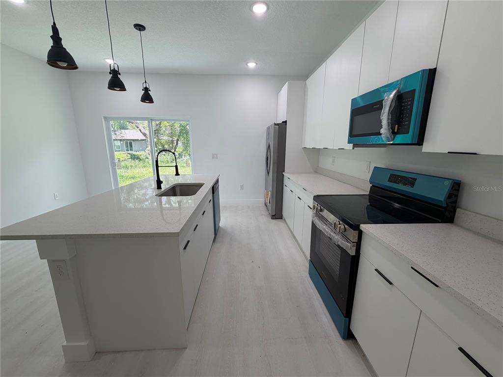 A modern kitchen features white cabinets, quartz countertops, a center island, and stainless steel appliances — 13542 SW 114TH PLACE, DUNNELLON, FL