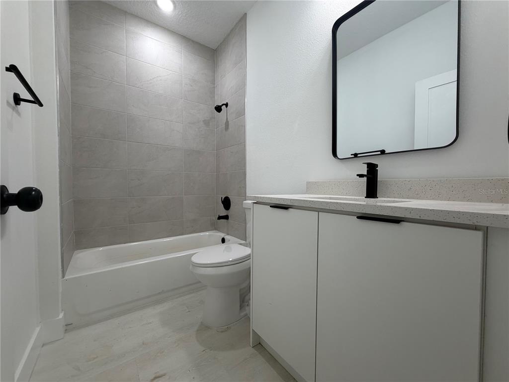 A modern bathroom features a tiled shower-tub combo, a white vanity, and a black-framed mirror — 13542 SW 114TH PLACE, DUNNELLON, FL
