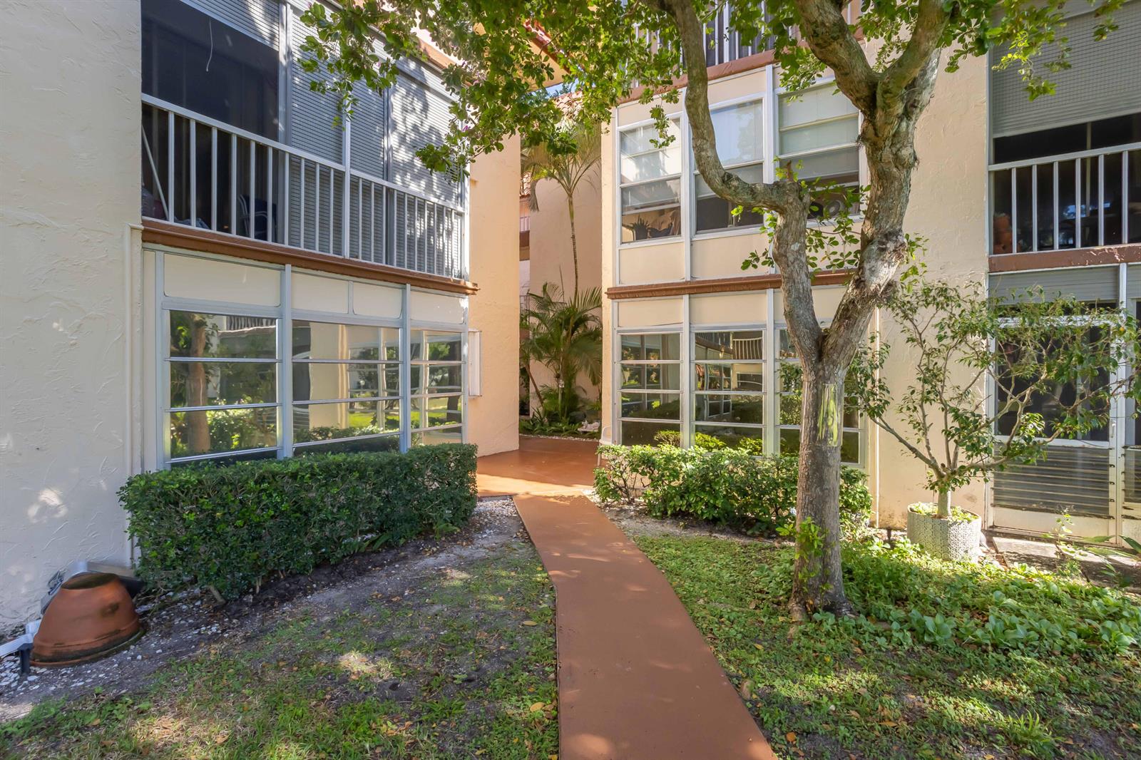 A paved walkway leads between two multi-story apartment buildings with balconies and large windows — 700 SE 6th Avenue # 107, Deerfield Beach FL 33441, DEERFIELD BEACH, FL