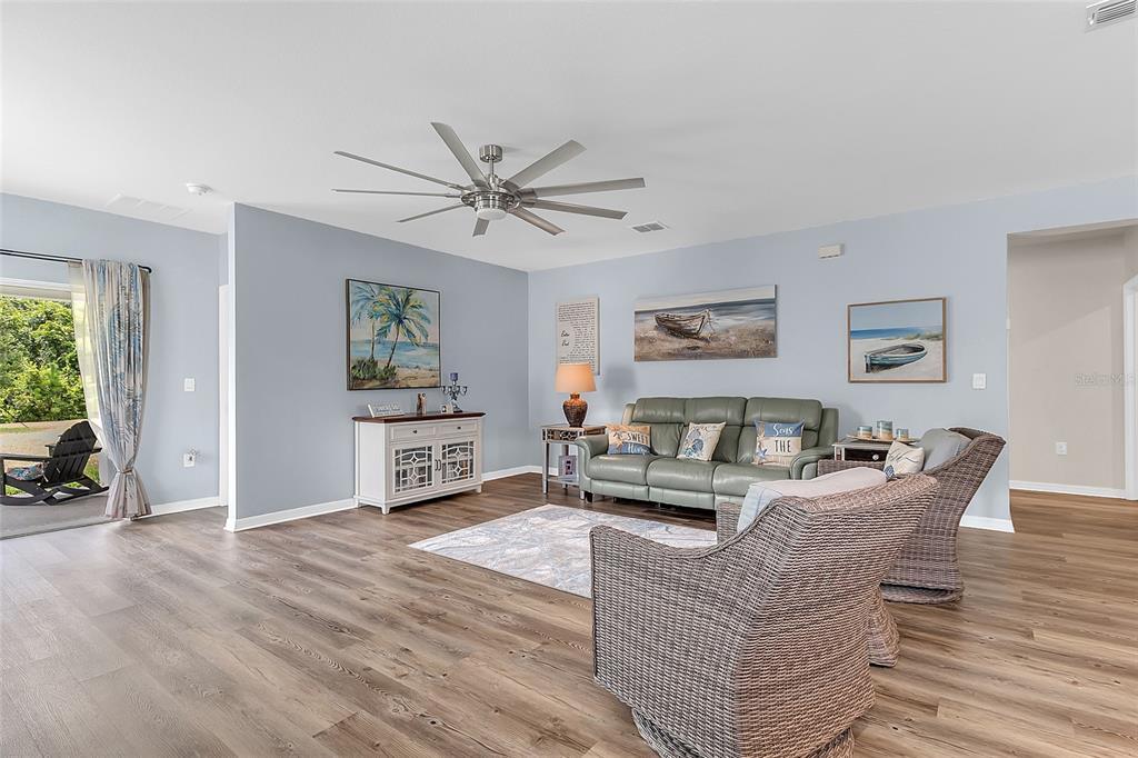 A living room features light blue walls, wood-look flooring, a ceiling fan, and coastal decor — 3241 CARPENTARIA DRIVE, NEW SMYRNA BEACH, FL