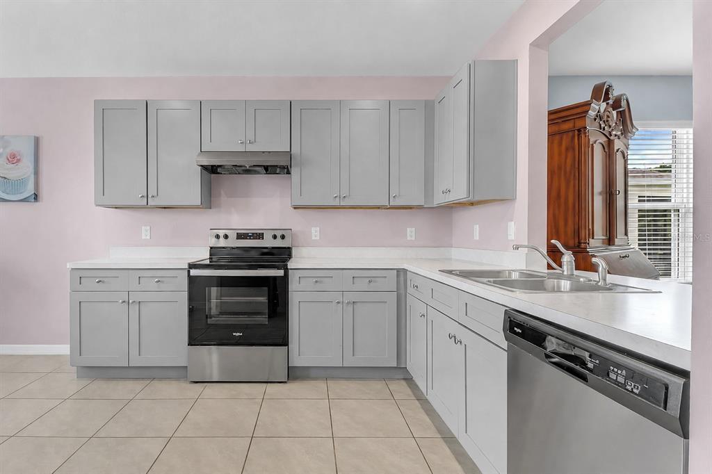 A kitchen features light gray cabinets, stainless steel appliances, white countertops, and light tile flooring — 3241 CARPENTARIA DRIVE, NEW SMYRNA BEACH, FL