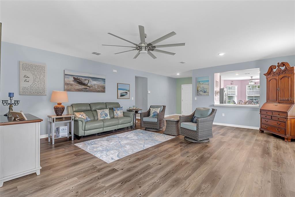 A living room features light blue walls, wood-look flooring, a ceiling fan, and coastal decor — 3241 CARPENTARIA DRIVE, NEW SMYRNA BEACH, FL
