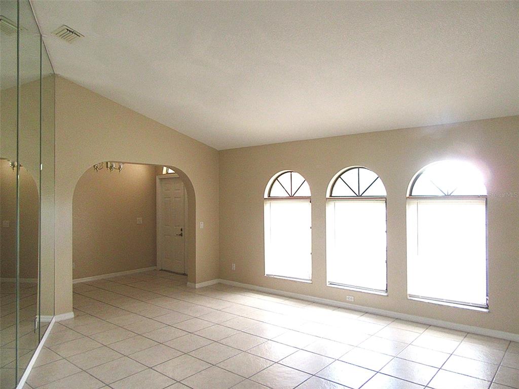 A living room with tiled floors, vaulted ceilings, arched windows, and a mirrored wall — 22182 PEACHLAND BOULEVARD, PORT CHARLOTTE, FL